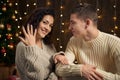 The man gives the girl an engagement ring, couple is in christmas lights and decoration, dressed in white, fir tree on dark wooden Royalty Free Stock Photo