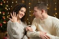 The man gives the girl an engagement ring, couple in christmas lights and decoration, dressed in white, fir tree on dark wooden ba Royalty Free Stock Photo