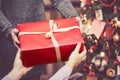 Man is giving a big red gift box to a woman against amazing christmas tree background. Toned and selective focus Royalty Free Stock Photo