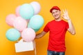 Man giving food order cake box on yellow background. Male employee courier in red cap t-shirt hold colorful air