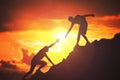 Man is giving helping hand. Silhouettes of people climbing on mountain at sunset