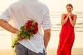 Man giving roses to his surprise and wonder woman on the ocean beach. romantic date or wedding or valentines day concept