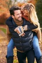 Man Giving Woman Piggyback  As Loving Couple Walking Along Autumn Woodland Path Through Trees Royalty Free Stock Photo