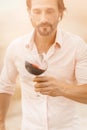 Man with glass of red wine. Bearded caucasian man in a white shirt holds a glass of red wine looking on it. Winetasting Royalty Free Stock Photo