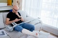 A man with glasses with a broken leg is sitting on the couch at home. Calls the insurer for compensation.