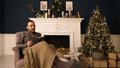 A man in glasses in chair reading a book at home at Christmas time out loud. Christmas iterior.