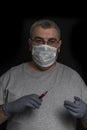 Man with glasses and a disposable mask and disposable gloves holds a syringe with red liquid Royalty Free Stock Photo