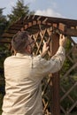 Man with glasses and a flannel shirt during spring gardening. Renovation and maintenance of garden pergolas. The man`s hand tigh