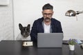 Man with glasses freelance working from home with his dog sitting together at workspace