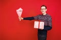 A man in glasses holds a gift and holds out a bouquet of flowers on a red background Royalty Free Stock Photo