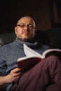 A man with glasses is reading a book. Middle-aged man of ordinary appearance in casual clothes at home. Reading, learning Royalty Free Stock Photo