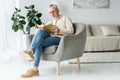 Man in glasses reading book while sitting in armchair at home Royalty Free Stock Photo