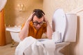 Man in glasses sits resting his hands on toilet