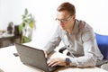 A man with glasses is sitting in an office and typing on a laptop keyboard. Businessman at work