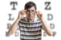 Man with glasses is testing his sight. Chart for eye sight testing in background