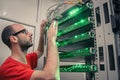 A man with glasses works in the server room. Young engineer switches wires in a rack with telecommunication equipment. The Royalty Free Stock Photo