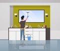 Man in gloves and apron cleaning mirror with squeegee guy doing housework concept modern bathroom interior rear view