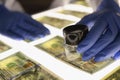 Man in gloves checking counterfeit money with magnifying glass closeup