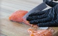 Man in gloves cuts fish into slices.Piece of fresh raw salmon on board