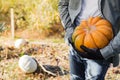 Man in gloves holds a yellow pumpkin in field at sunset in autumn harvest time. Pumpkin patch. Happy Thanksgiving and Halloween Royalty Free Stock Photo