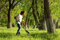 A man in gloves is looking for a treasure in the ground with the help of a pinpointer in the spring forest.