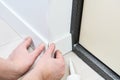 A man with glue glues floor MDF plinth.A man sets up white floor moldings in an apartment.Close view of man installing new skirtin