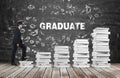 A man is going up using a stairs which are made of white books. The word graduate is on the black chalkboard. Royalty Free Stock Photo