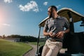 Man with golf ball in hand looking away while standing near golf cart Royalty Free Stock Photo