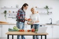 Man with gray beard pours chopped pieces of tomato into bowl held by partner.