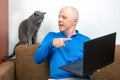 Man with a gray cat looks at a laptop screen. freelancer business works at home. relationship with a cat