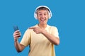 Man With Gray Hair Wearing Headphones Showing Smartphone, Blue Background Royalty Free Stock Photo