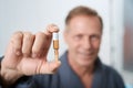 Man in hospital gown holds ampoule of medicine in his hands