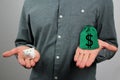 Man in a gray shirt in one hand holds a green bag with a dollar symbol, in the other a small white piggy bank, the concept of Royalty Free Stock Photo