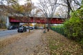 A man with a gray shirt running on a sidewalk covered in fallen autumn leaves surrounded by autumn colored trees and parked cars