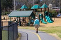 A man in a green shirt wearing a hat walking along a winding footpath in the park near a brown and green jungle gym