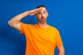 A man in greeting pose and serious face. A hispanic man with a beard wearing orange t-shirt isolated on blue background Royalty Free Stock Photo