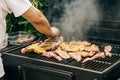 Man grilling meat on a barbecue various types of meat, chicken, sausages, blood sausage, lamb on a crbon grill in the garden