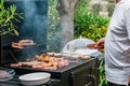 Man grilling meat on a barbecue various types of meat, chicken, sausages, blood sausage, lamb on a crbon grill in the garden