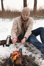 Man grilling sausages at campfire in winter