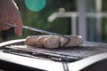 Man grilling and turning German Bratwurst pork sausage with metal tong on electric barbecue BBQ grill Royalty Free Stock Photo