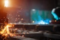 A man grinds metal. In the background a welder welds a part