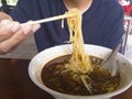 A man is gripping noodles with chopsticks from the white bowl of