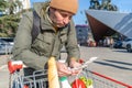 Man with a grocery cart outdoors, reviewing a shopping list, with fresh produce visible in the cart Royalty Free Stock Photo