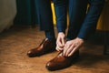 A man or a groom in a blue suit ties up shoelaces on brown leather shoes brogues on a wooden parquet background Royalty Free Stock Photo