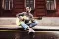 Man with guitar sits on road border