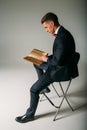 A man, a guy in a blue suit, sits on a chair and reads an old book, the concept of knowledge, study, science, business, everything Royalty Free Stock Photo