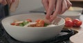 Man hand adds chicken slices on salad with romaine and tomatoes in white bowl