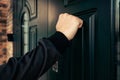 man hand in a black jacket knocks on a dark green wooden door. Anybody home. Royalty Free Stock Photo