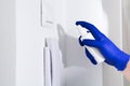 Man hand in blue glove cleaning door phone with sanitizer