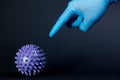 A man hand in a blue medical glove scares and threatens by pointing finger purple virus ball on a black background